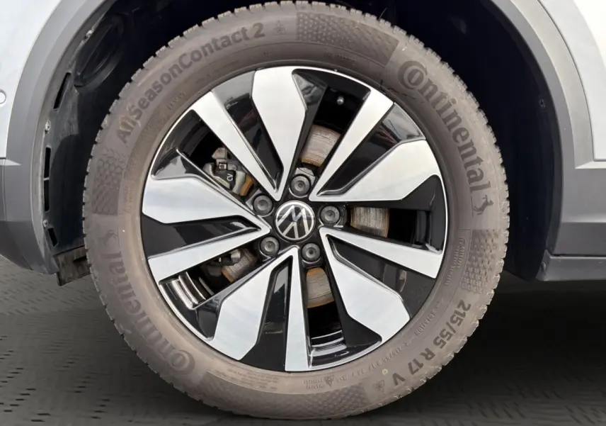 Gros plan sur la roue avant droite du Volkswagen T-Roc gris clair, jante alliage bicolore avec logo VW central.