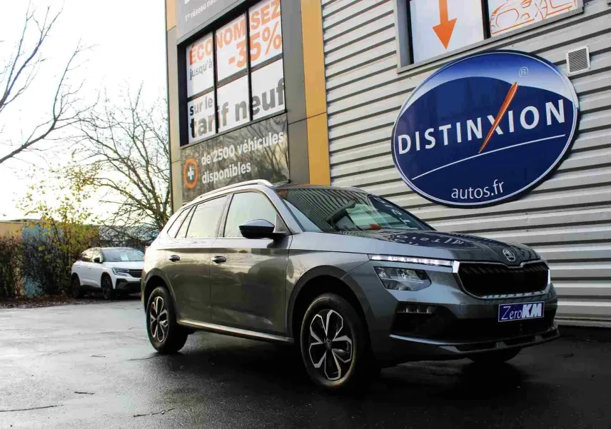 Skoda Kamiq gris graphite vu de trois quarts avant droit, stationné devant un mur avec logo Distinxion.