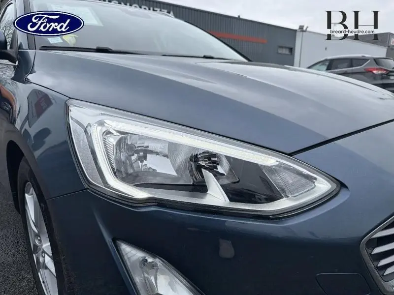 Gros plan sur le phare avant droit d’une Ford Focus SW 1.5 EcoBlue bleu azur métallisé, avec calandre partielle visible.