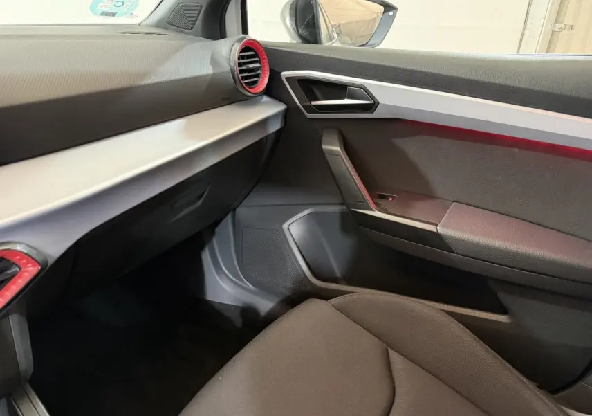 Intérieur SEAT Ibiza 2024 blanc, vue côté passager avant, tableau de bord gris avec aérateurs rouges.
