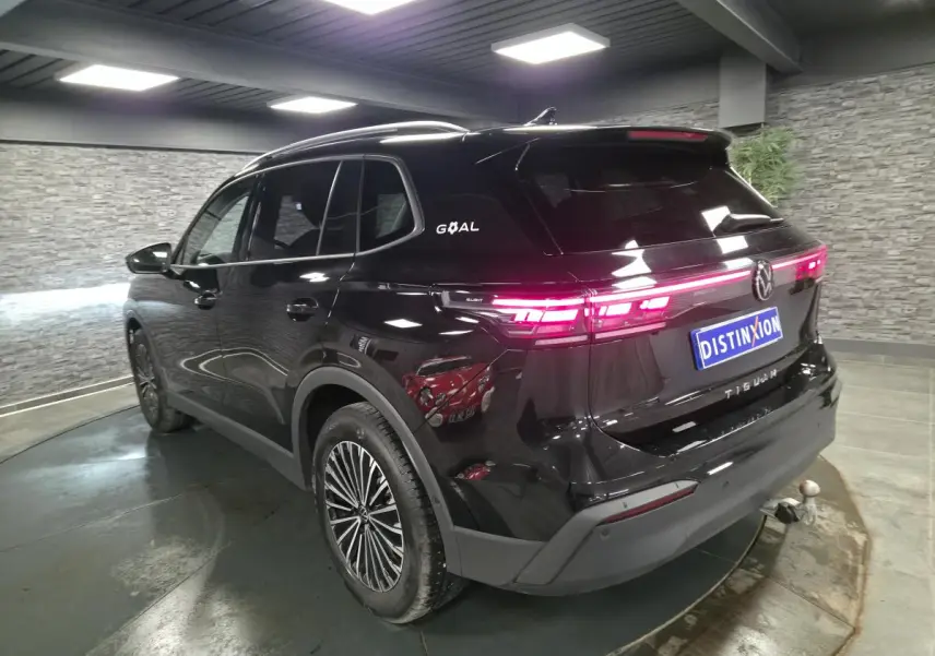 Vue 3/4 arrière droite du Volkswagen Tiguan noir avec feux arrière allumés et crochet d'attelage visible.