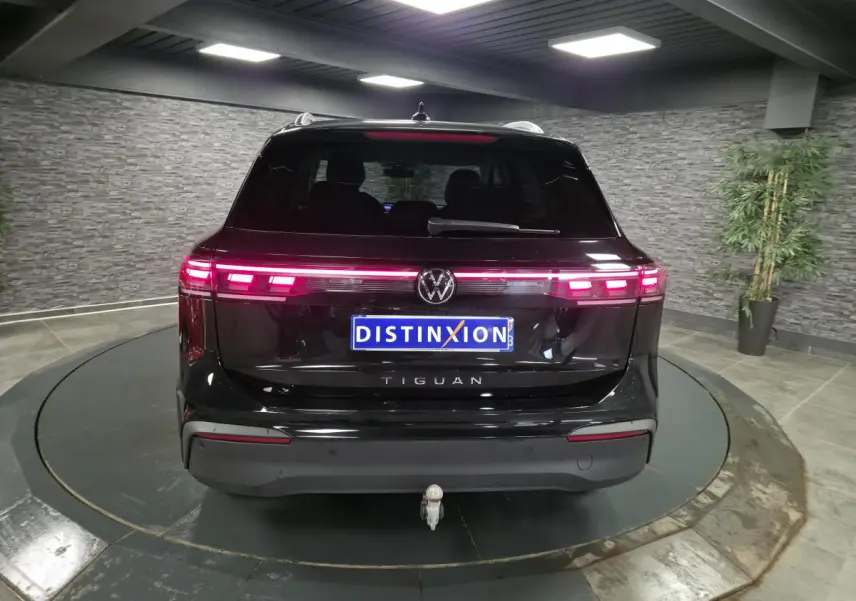 Vue arrière d'un Volkswagen Tiguan noir 2025 avec feux LED allumés et crochet d'attelage escamotable visible.