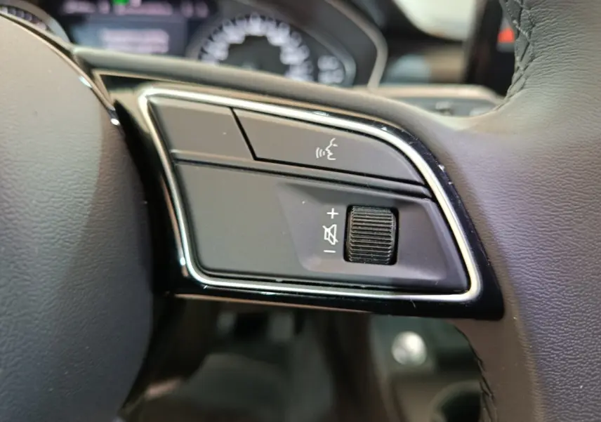 Gros plan sur les commandes vocales et volume au volant cuir noir de l'Audi A4 35 TFSI Business Line 2024.