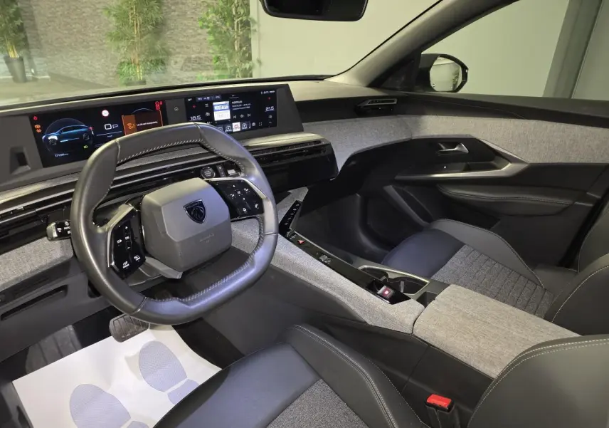 Vue intérieure côté conducteur du Peugeot 3008 gris 2025, avec tableau de bord numérique et sellerie tissu gris chiné.
