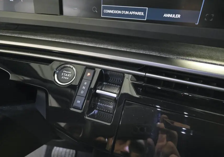 Gros plan sur la console centrale noire laquée du Peugeot 3008 Hybrid 2025 avec bouton start/stop et commande de boîte auto.