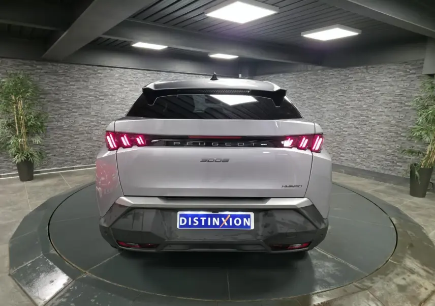 Vue arrière d'un Peugeot 3008 gris métallisé avec feux LED 3 griffes et bandeau noir laqué entre les feux dans un showroom.