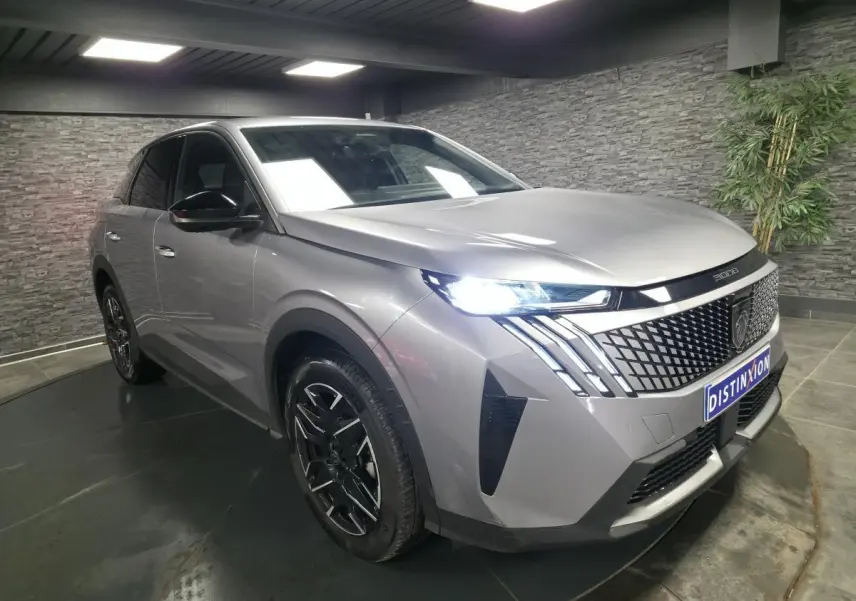 Peugeot 3008 gris métallisé en 3/4 avant droit, avec calandre noire et phares LED allumés dans un showroom.