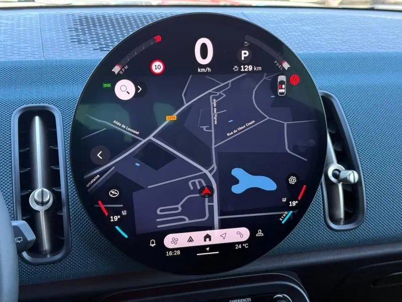 Vue rapprochée du tableau de bord numérique circulaire du MINI Countryman 2024, affichant la navigation et la température intérieure.