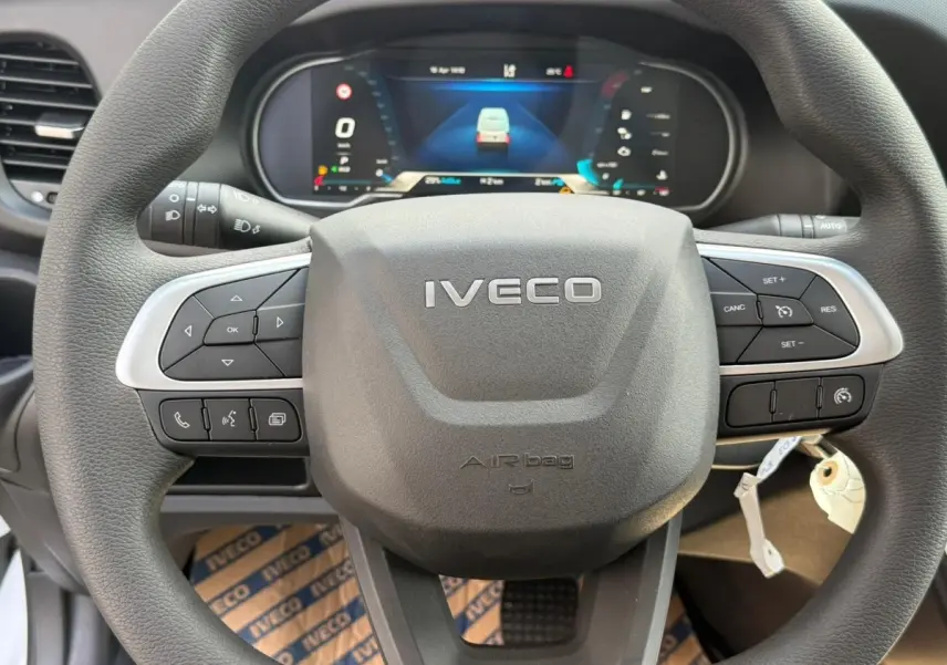 Vue rapprochée du volant gris foncé de l'Iveco Daily 2026 avec commandes intégrées et tableau de bord numérique en arrière-plan.