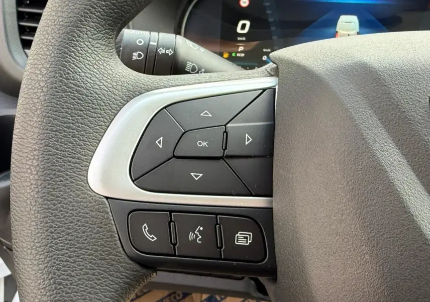 Gros plan sur les commandes gauche du volant noir du Iveco Daily blanc, avec affichage digital en arrière-plan.