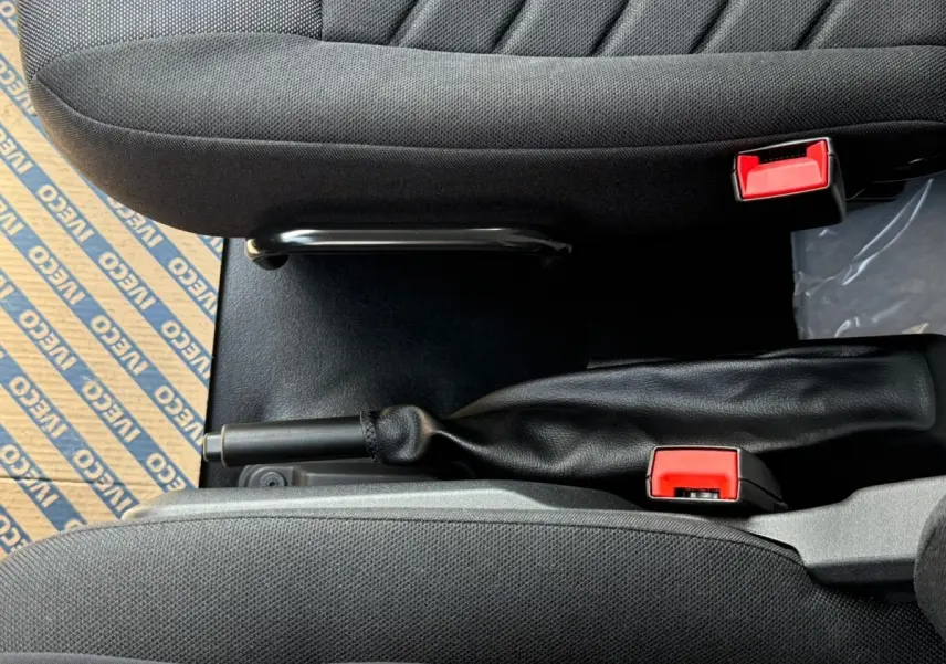 Vue rapprochée de la console centrale intérieure du Daily IVECO blanc, montrant le frein à main et les ceintures de sécurité rouges.