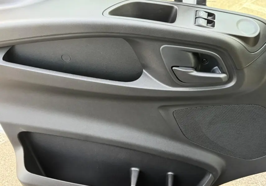 Intérieur de la porte côté conducteur du Iveco Daily blanc 2026, avec poignée, commandes de vitre et haut-parleur intégrés.