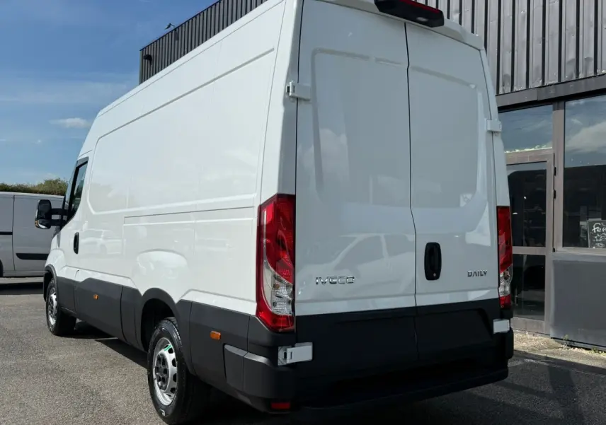 Vue 3/4 arrière droite d’un utilitaire Iveco Daily blanc avec portes arrière fermées et feux rouges visibles.