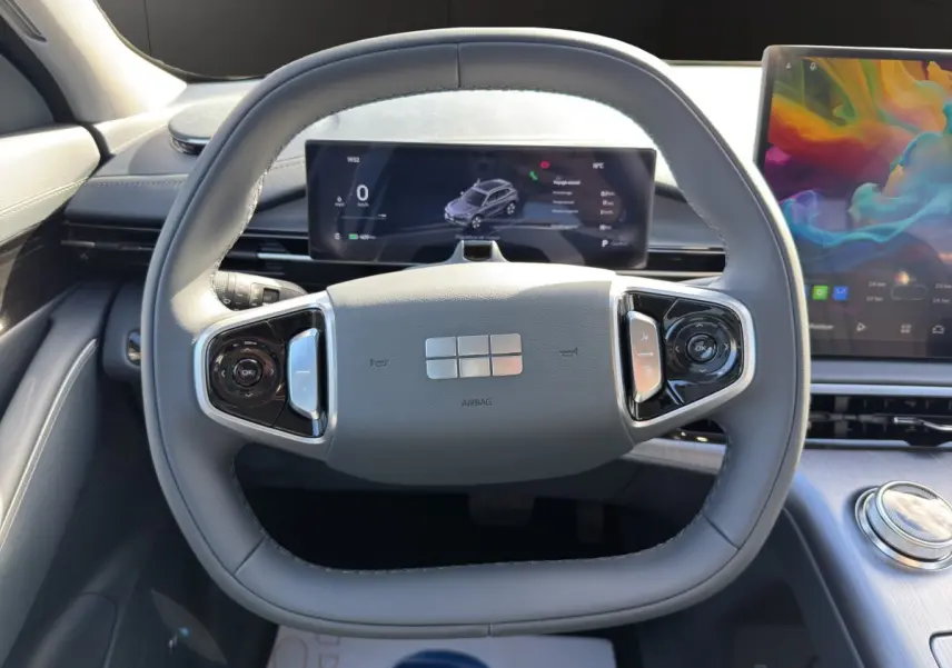 Vue intérieure centrée sur le volant gris clair du Geely E5 2026 avec tableau de bord numérique et écran tactile coloré.