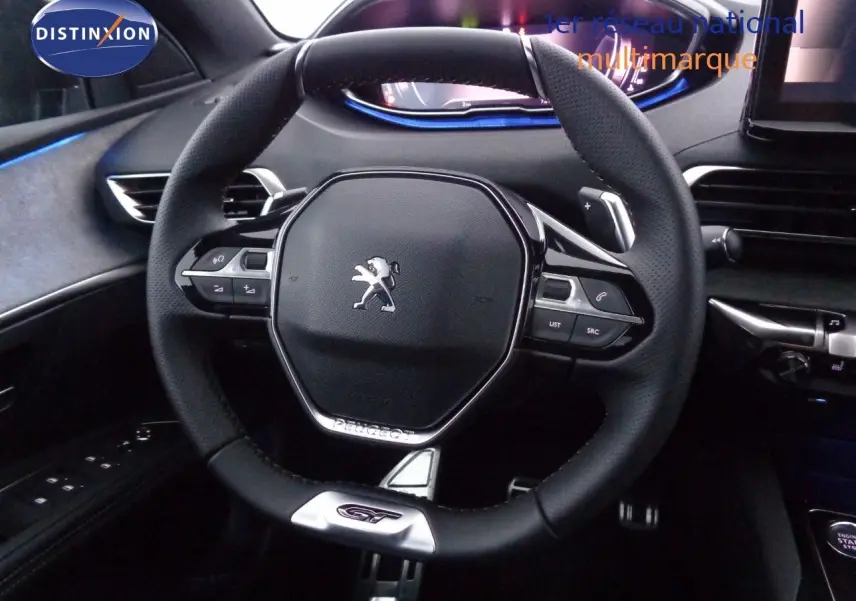 Vue rapprochée du volant cuir noir avec logo Peugeot et badge GT du Peugeot 3008 2023, intérieur moderne et éclairage bleu.