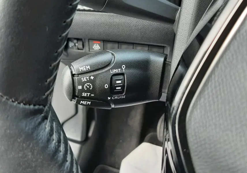 Gros plan sur la commande de régulateur de vitesse noire à gauche du volant d'un Peugeot 2008 gris 2021.