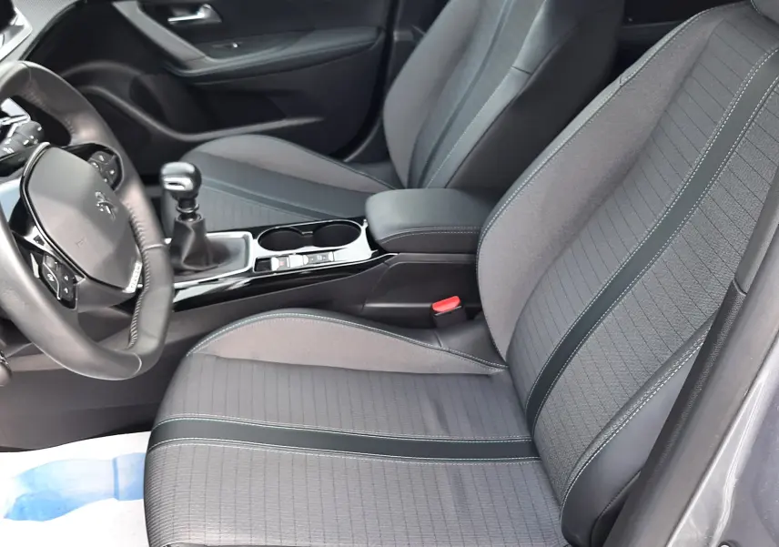 Vue intérieure côté conducteur du Peugeot 2008 gris 2021, sièges tissu gris avec surpiqûres et levier de vitesse manuel.