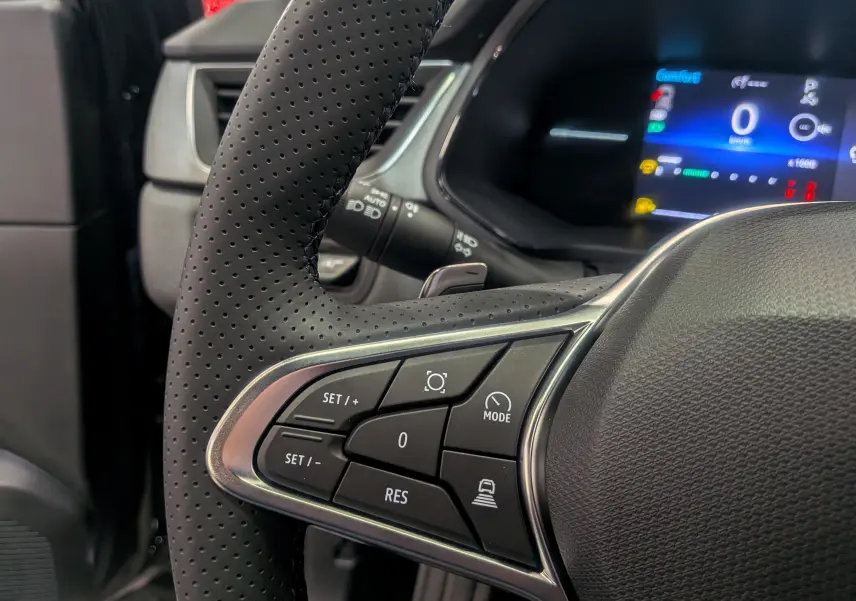 Gros plan sur le volant noir perforé du Renault Captur 2025 avec commandes intégrées et tableau de bord numérique en arrière-plan.