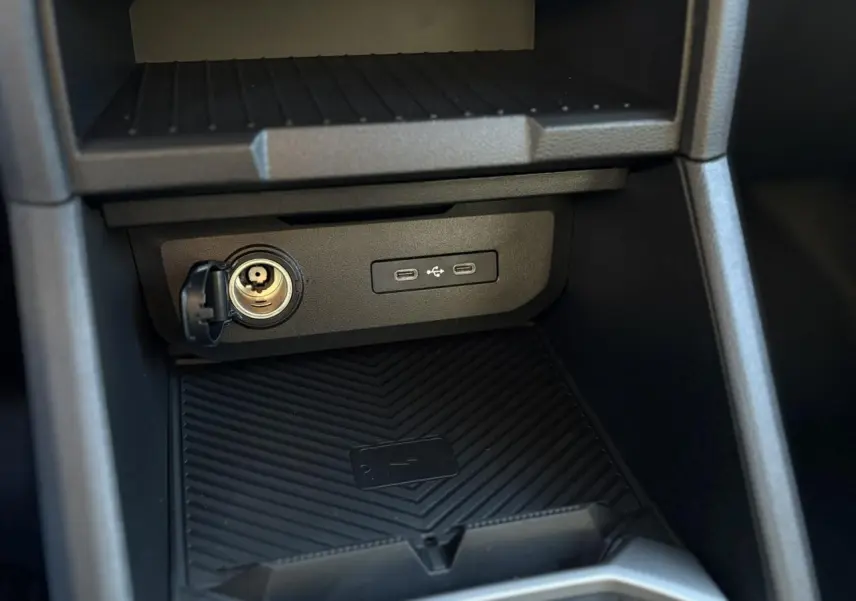 Gros plan sur la console centrale du Dacia Duster 2026, montrant prise allume-cigare, ports USB et zone de charge sans fil.