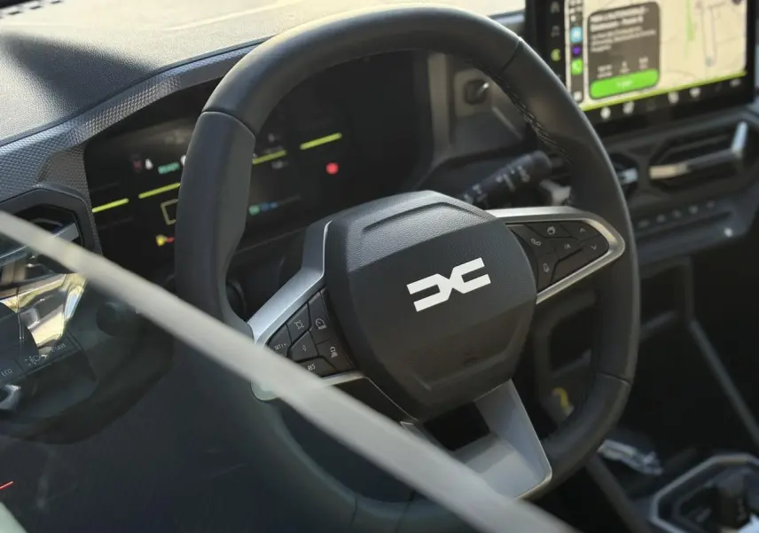 Gros plan sur le volant noir du Dacia Duster 2026 avec tableau de bord digital et écran tactile visible en arrière-plan.