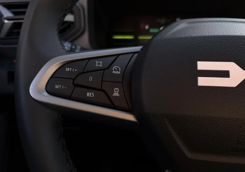 Gros plan sur les commandes gauche du volant noir du Dacia Duster 2026, avec logo Dacia visible au centre.