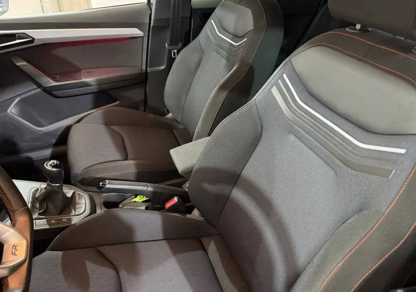 Vue intérieure côté conducteur de la SEAT IBIZA 1.0 TSI 110 FR 2024 noire, sièges sport avec surpiqûres orange et volant multifonction cuir alu.