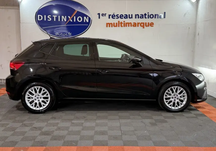 Profil droit d'une SEAT Ibiza 1.0 TSI 110 FR noire, avec jantes alliage argent et vitres teintées, en intérieur showroom.