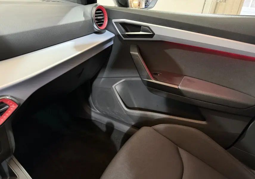 Intérieur côté passager de la SEAT Ibiza 1.0 TSI 110 FR 2024, avec tableau de bord noir et cerclage rouge des aérateurs.