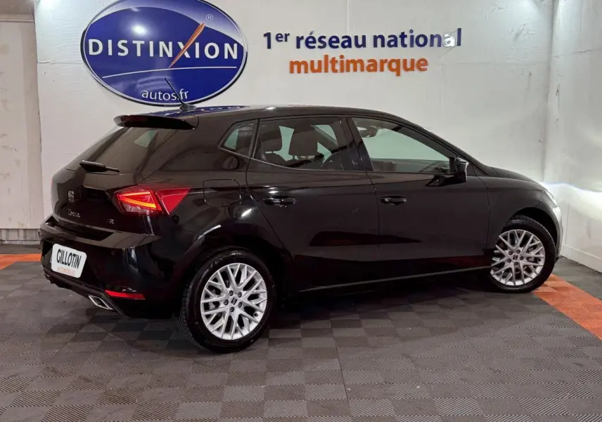 Vue 3/4 arrière droite d'une SEAT Ibiza noire 2024 avec jantes alliage et feux arrière LED allumés.