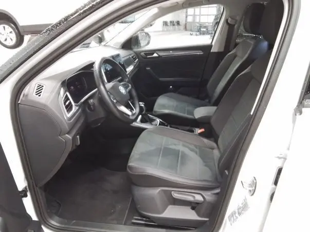 Vue intérieure côté conducteur du Volkswagen T-Roc blanc toit noir 2025, mettant en valeur les sièges et le tableau de bord moderne.