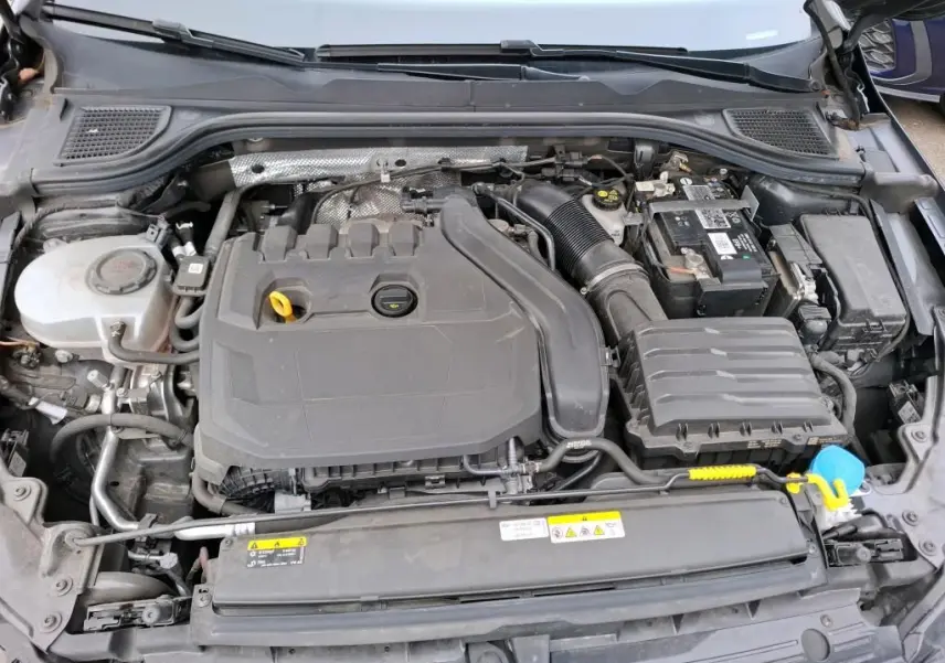 Vue plongeante sur le moteur essence gris d'une Volkswagen Golf 1.5 eTSI 130 DSG7 Active, avec batterie et réservoir visibles.