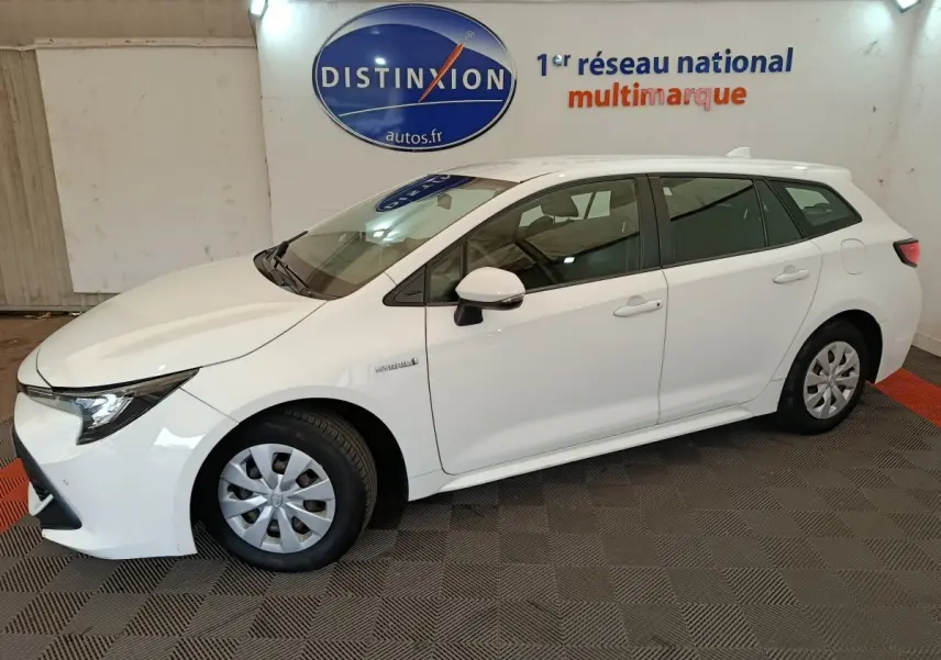 Vue de profil côté gauche d'une Toyota Corolla Hybride 122h Active blanche en version break, stationnée en intérieur showroom.