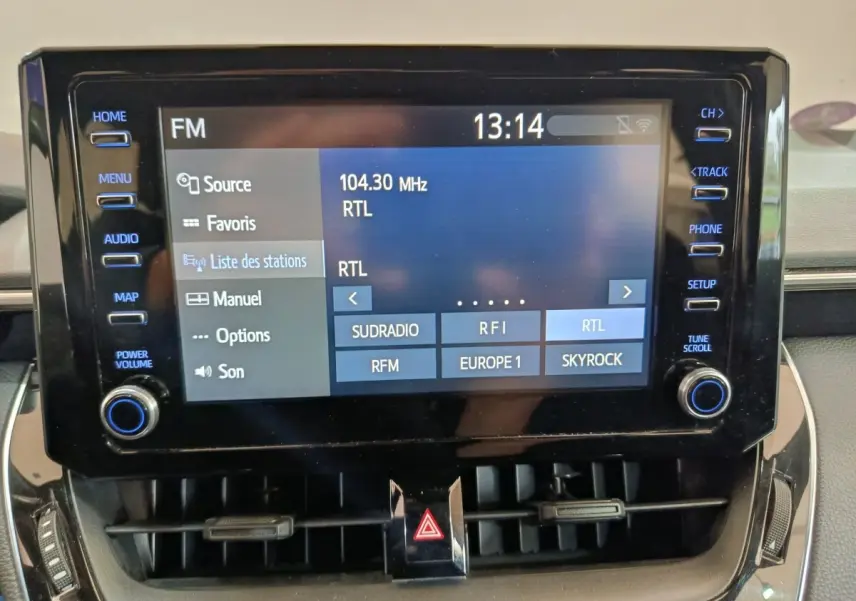 Écran tactile central de la Toyota Corolla Hybride 2020 affichant les stations radio FM, entouré de boutons de commande.