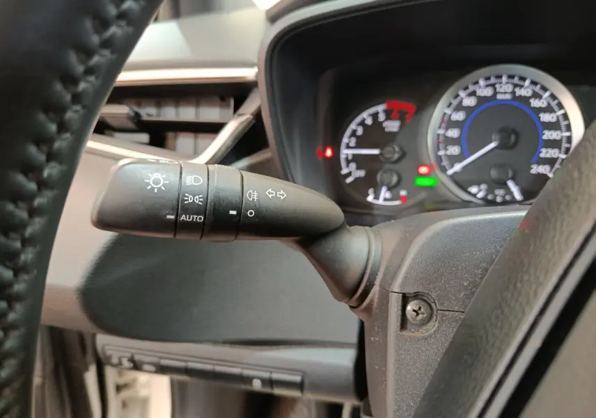 Gros plan sur la manette des phares et clignotants à gauche du volant dans le tableau de bord d'une Toyota Corolla hybride.