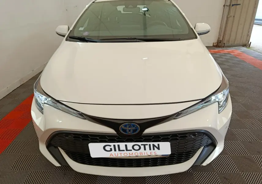 Vue avant d'une Toyota Corolla Hybride 122h Active blanche avec calandre noire et logo bleu Toyota visible.