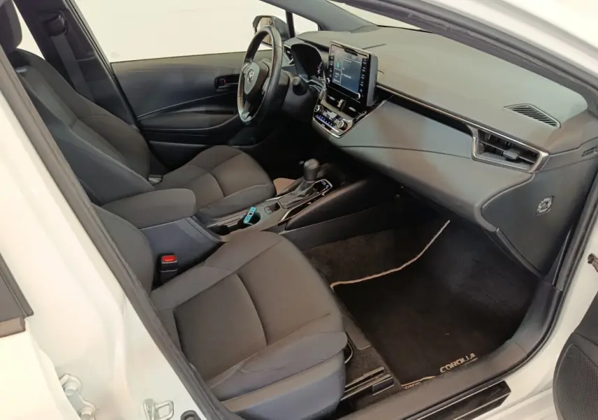Intérieur avant droit de la Toyota Corolla Hybride blanche, montrant sièges noirs et tableau de bord avec écran tactile central.