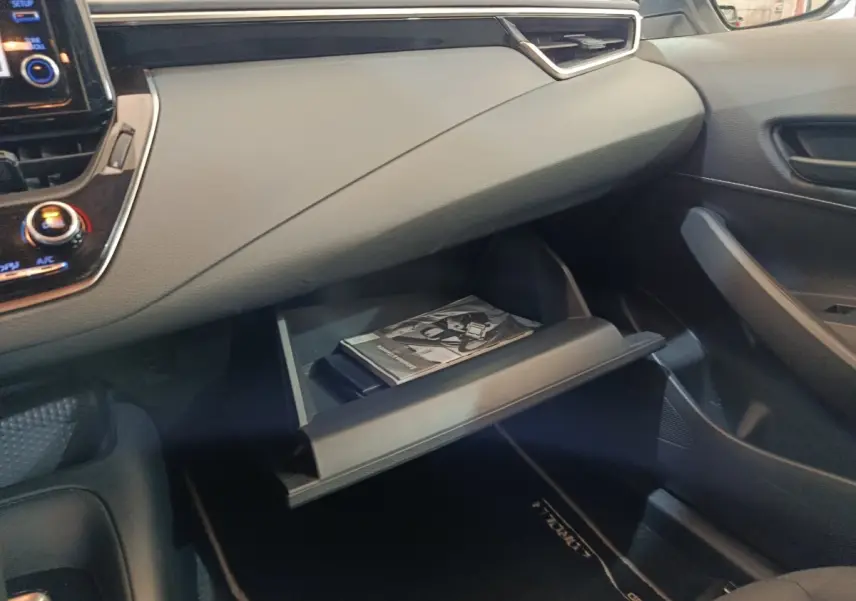 Vue intérieure côté passager de la boîte à gants ouverte de la Toyota Corolla Hybride 122h Active avec manuel visible.