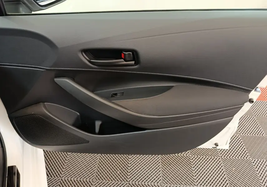 Gros plan sur la porte intérieure côté gauche noire de la Toyota Corolla Hybride 122h Active blanche, avec poignée et haut-parleur intégrés.