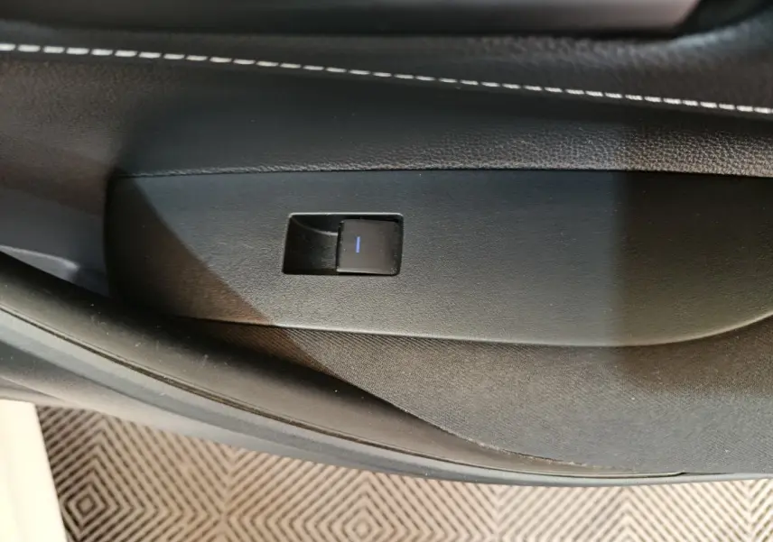 Gros plan sur le bouton de commande de lève-vitre côté porte intérieure noire de la Toyota Corolla Hybride blanche 2020.
