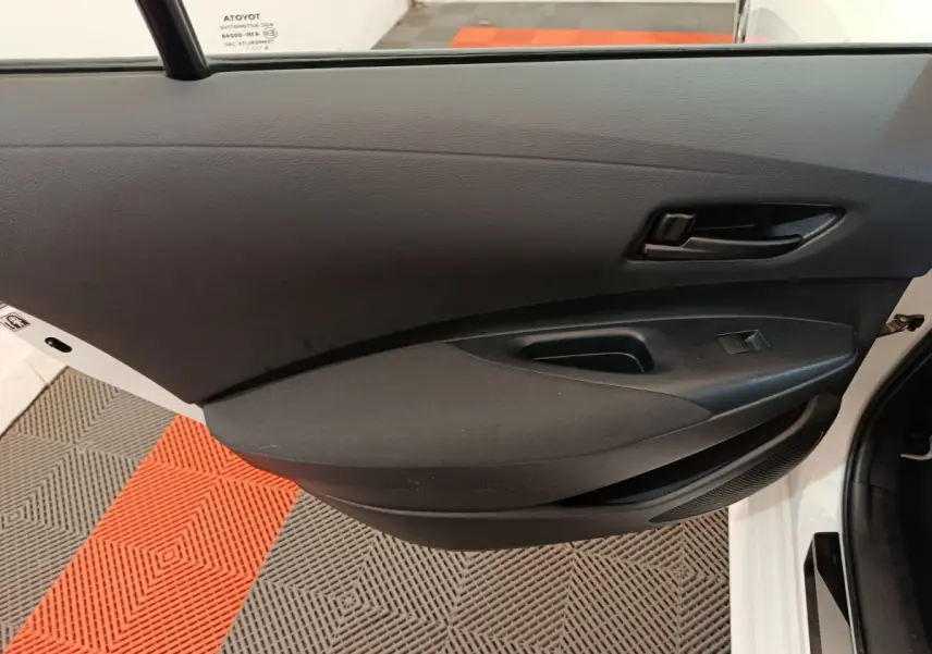 Vue rapprochée de la porte avant gauche noire intérieure d’une Toyota Corolla Hybride blanche, avec poignée et commande de vitre.