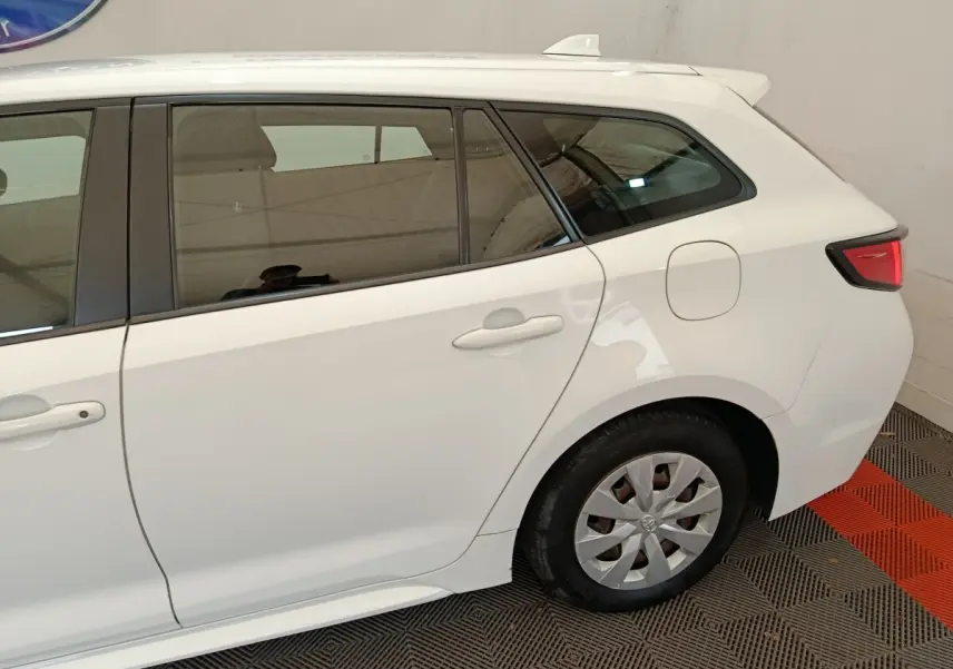 Vue latérale côté gauche sur l'arrière d'une Toyota Corolla hybride blanche avec feux arrière LED et jante acier.