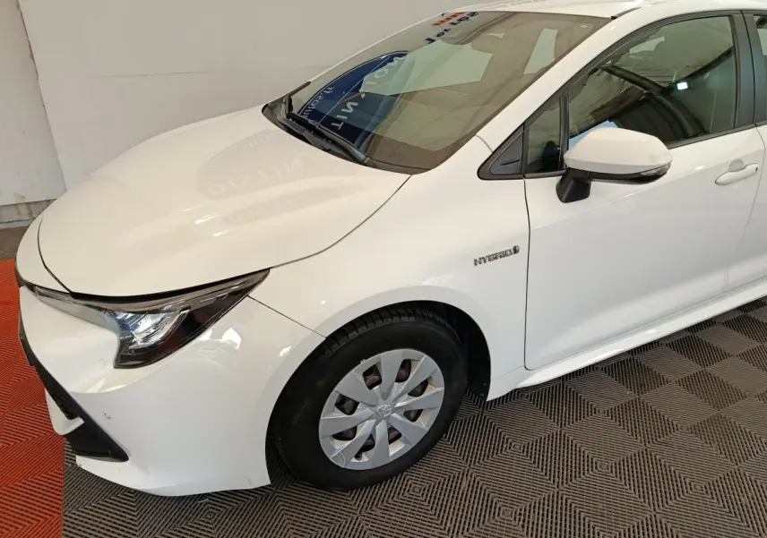 Vue 3/4 avant droit d'une Toyota Corolla Hybride 122h Active blanche, avec badge Hybrid visible sur l'aile avant.