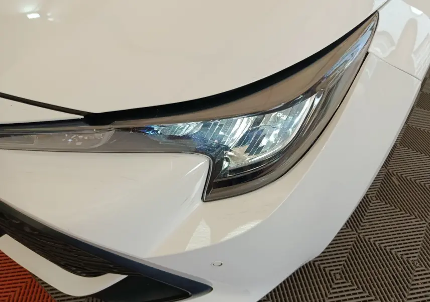 Gros plan sur le phare avant droit blanc d'une Toyota Corolla Hybride 122h Active 2020, avec détails du pare-chocs.