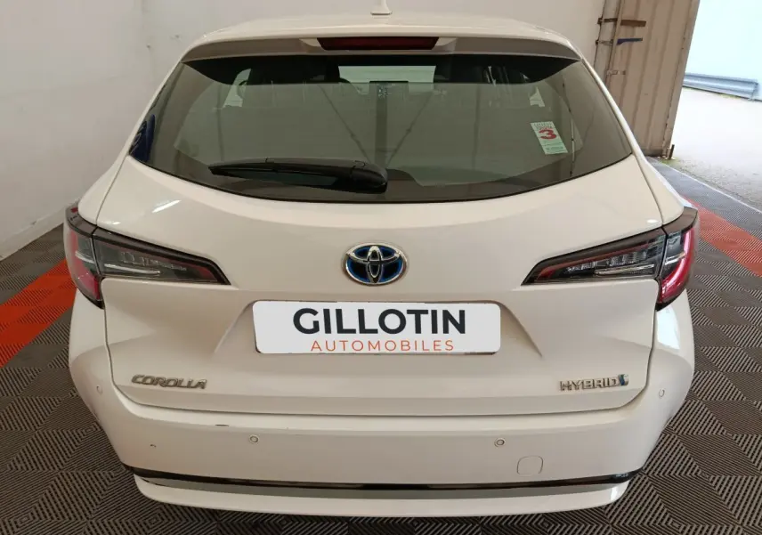 Vue arrière d'une Toyota Corolla Hybride blanche 2020, avec feux LED et logo Toyota visible sur un sol à damier noir et rouge.