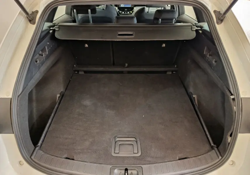 Coffre ouvert vu de l'arrière d'une Toyota Corolla Hybride blanche, avec cache-bagages en place et intérieur noir.