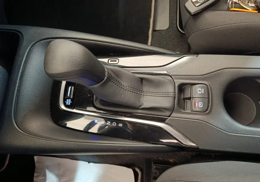 Vue rapprochée de la console centrale noire de la Toyota Corolla Hybride 2020 avec levier de vitesse automatique et boutons de frein à main électrique.