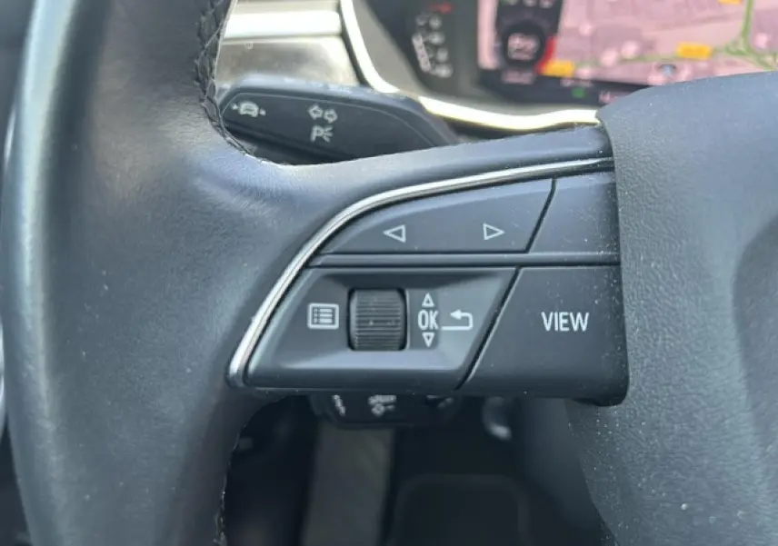 Gros plan sur les commandes gauche du volant cuir noir de l'Audi Q3 Sportback blanc, avec boutons de navigation et affichage.