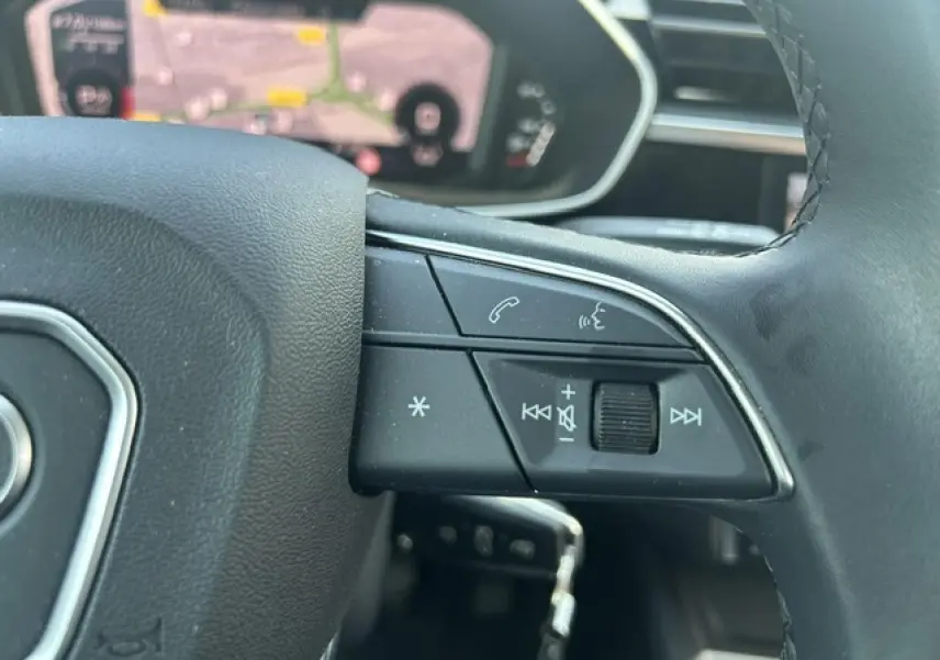 Gros plan sur les commandes gauche du volant cuir noir de l'Audi Q3 Sportback blanc avec affichage numérique en arrière-plan.