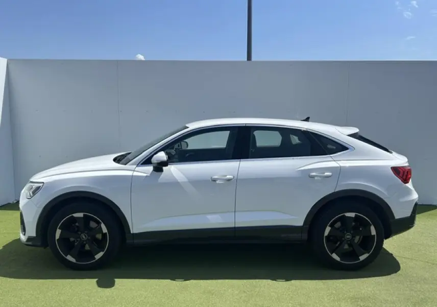 Profil droit d'un Audi Q3 Sportback blanc 2022 avec jantes noires et toit plongeant, sur fond extérieur clair.