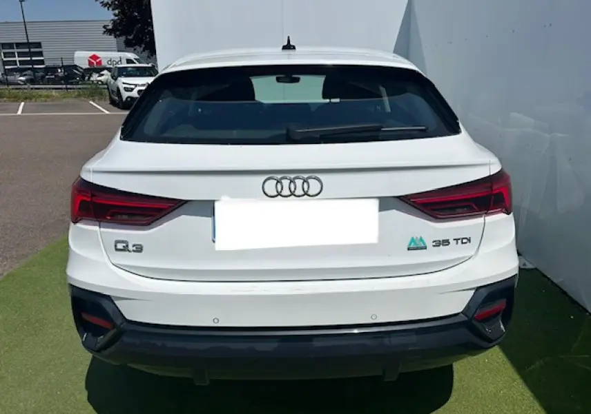 Vue arrière d'un Audi Q3 blanc 35 TDI avec feux LED et logo distinctif sur un parking extérieur.